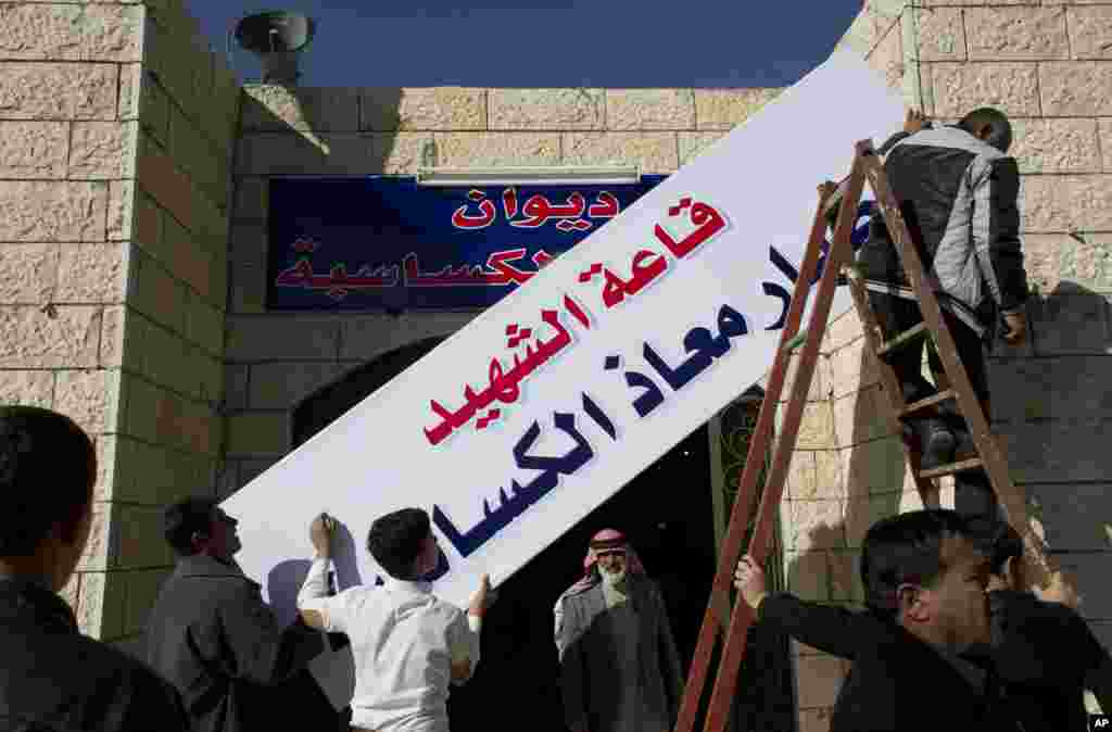 Workers hang a banner in Arabic that reads, "the hall of martyr pilot Muath al-Kaseasbeh," over the entrance of the tribe's gathering divan, at his home village of Ai, near Karak, Feb. 4, 2015.