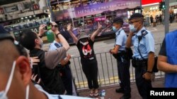 Mwanamke akitoa ishara wakati maafisa wa polisi walipomsimamisha kumpekua Juni 4, 2021, nje ya bostanı ya Victoria Park katika maadhimisho ya 32 ya kamatakamata ya waandamanaji waliokuwa wanaunga mkono demokrasia katika eneo la Tiananmen Square huko Beijing 1989. REUTERS/Lam Yi