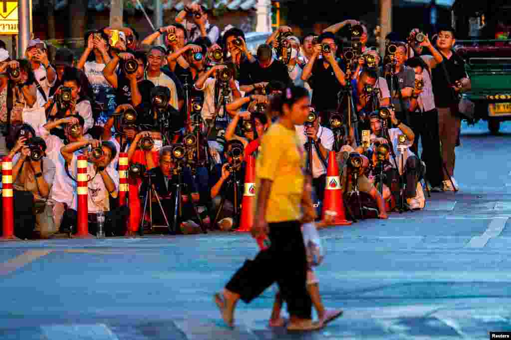 People cross a street, as photographers take pictures of the sunset behind the Giant Swing, also known as Sao Chingcha, in Bangkok, Thailand.