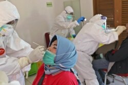 A health worker collects nasal swab samples from a woman during a mass test for the new coronavirus in a neighborhood in Tangerang, Indonesia, July 17, 2020.