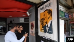 Des Tunisiens regardent une affiche du film "Papa Hedi, l'homme au microphone" dédiée au grand chanteur tunisien Hedi Jouini, à Tunis, le 23 octobre 2018.