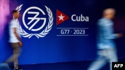 Hombres caminan cerca de un cartel de la Cumbre del G77 + China durante la inauguración de la sala de prensa en La Habana, el 13 de septiembre de 2023