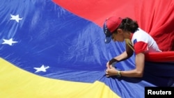 Una partidaria del líder opositor venezolana Juan Guaidó, fija una bandera durante un mitin contra el gobierno del presidente venezolano Nicolás Maduro en Caracas. Abril 6, 2019.