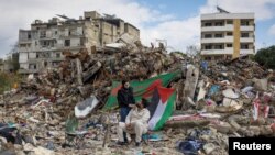 Еден ден по прекинот на огнот меѓу Израел и Хезболах, двајца мажи седaт во близина на урнатините на зграда каде што нивното семејство имало продавница во јужен либански град (28 ноември 2024 г.)