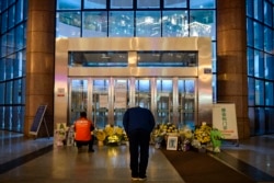 FILE - This photo taken Feb. 7, 2020, shows a man bowing in front of flowers and a photo of the late ophthalmologist Li Wenliang outside the Houhu Branch of Wuhan Central Hospital in Wuhan, Hubei province, China.