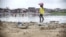 A woman wades near a beach in Monrovia, Liberia. Though poverty does not discriminate, women have fewer resources to cope. 
