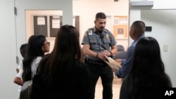 Un agente les da indicaciones mientras escucha a varias personas para llegar a uno de los tribunales en una corte de migración en Miami, Florida, el 10 de enero de 2024.