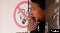 FILE - A man smokes in front of a "no smoking" sign outside a shopping mall in Shanghai, Jan. 10, 2014.