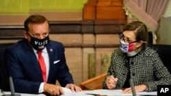 Buramatari wa reta ya Iowa, Kim Reynolds iburyo, n'umunyamabanga mukuru w'iyo reta Paul Pate, ibubamfu baharura amajwi y'intumwa zihagarariye abatoye, kw'italiki 14/12/2020 i Des Moines, Iowa.