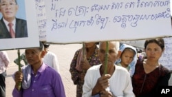 Sam Souen, an 86 year-old Cambodian woman, holds a banner asking Prime Minister Hun Sen, seen in photo at left, to help solve the problem of land grabbing, which reads "We have been victimized by land grabbing in Banteay Meanchey province" as she and othe