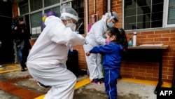 Una maestra con equipo de protección personal verifica la temperatura de un niño durante la apertura de los jardines de infancia en Bogotá, el 23 de septiembre de 2020 en medio de la pandemia del coronavirus COVID-19.