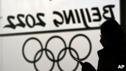 A woman looks at her phone as she passes an Olympic logo inside the main media center for the Beijing Winter Olympics Tuesday, Jan. 18, 2022, in Beijing. (AP Photo/David J. Phillip)