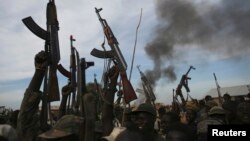 Rebel fighters hold up their rifles as they walk in front of a bushfire in a rebel controlled territory in Upper Nile State, South Sudan, Feb. 13, 2014. 