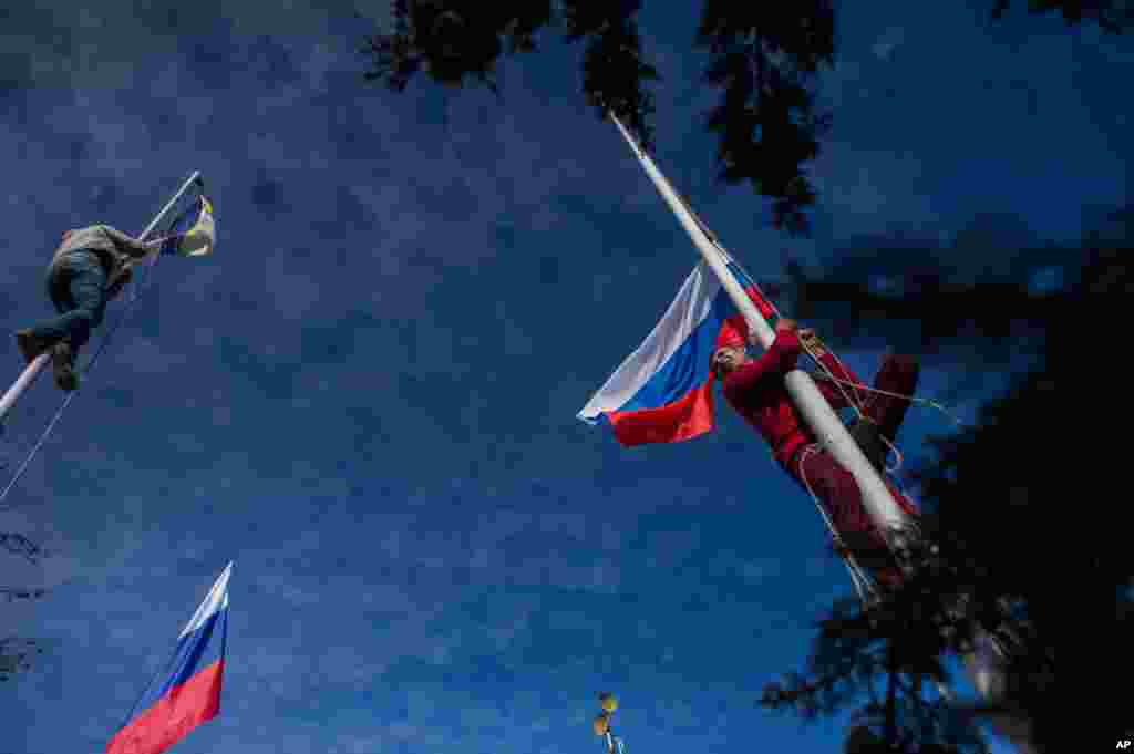 A member of a pro-Russian self-defense force takes down a Ukrainian Navy flag, left, as another raises the Russian flag at Ukrainian Navy headquarters in Sevastopol, Crimea, March 19, 2014.