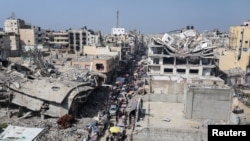 ဂါဇာရှိ အဆောက်အဦးပျက်များအနီး လမ်းဘေးစျေးတွင် သွားလာနေကြသည့် ပါလက်စတိုင်းလူမျိုးများ။ (မှတ်တမ်းရုပ်ပုံ)