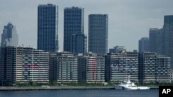 National banners hang from balconies at an athlete's village as Tokyo prepares for the 2020 Summer Olympics, Saturday, July 17, 2021. The pandemic-delayed games open on July 23 without spectators at most venues. (AP Photo/Charlie Riedel)