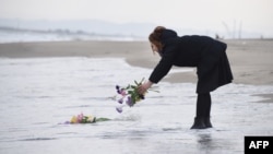 FILE - A woman puts flowers into the sea to pray for victims of the 2011 earthquake and tsunami in Sendai, northern Japan on the anniversary of the event. (AFP / TORU YAMANAKA)