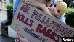 FILE - An environmental activist carrying a doll holds a placard outside the Central Jakarta Court in Jakarta, Indonesia, September 16, 2021.