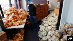 Volonter dovozi kolica s bananama, među džakovima sa doniranom hranom, dok stotine ljudi čeka u redu za hranu namenjenu onima koji su pogođeni epiemijom Kovida 19 u Čelsi, Masačuses, 28. aprila 2020. (AP Photo/Charles Krupa)