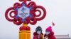 Dos mujeres, con mascarillas con el eslogan de los JJOO de Invierno de Beijing, se toman un selfie con una pieza decorativa instalada en la Plaza de Tiananmen con motivos de los Juegos, en Beijing, el 20 de enero de 2022. 