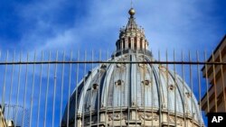 St. Peter's Dome is framed by the bars of the Perugino gate at the Vatican, Nov. 24, 2015. Two Italian journalists who wrote books detailing Vatican mismanagement faced trial on Tuesday in a Vatican courtroom along with three people accused of leaking the information in a case that has drawn scorn from media watchdogs.