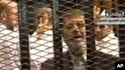 FILE - Video broadcast on Egyptian State Television shows ousted President Mohammed Morsi speaking from inside a mesh cage as he stands with other defendants during a court hearing at a police academy compound in Cairo, Egypt.