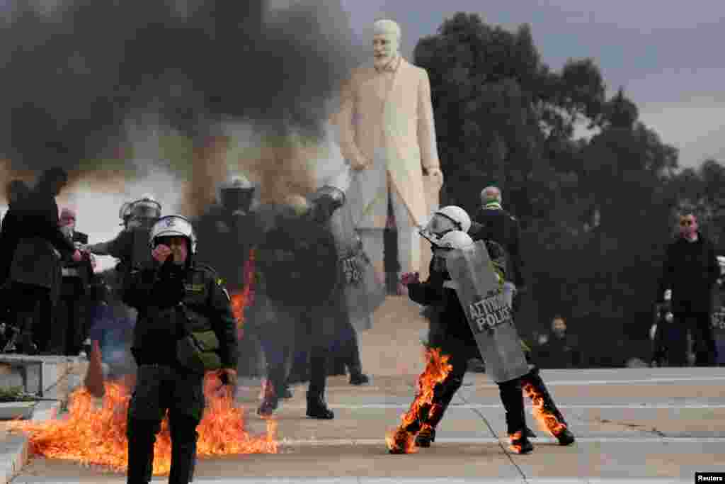 Riot police walk with their gear on fire, after being struck by Molotov cocktails at a protest near the Greek parliament, marking the second anniversary of the country's worst railway disaster, in Athens, Greece.