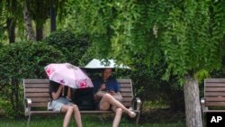 Dos mujeres se cubren del sol durante un día caluroso en Beijing, el 3 de julio de 2023. 