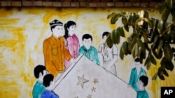 In this Sept. 20, 2018, photo, a mural showing Uighur and Han Chinese men and women carrying the national flag of China decorates the wall of a home at the Unity New Village in Hotan, in western China's Xinjiang region.