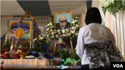 ស្ត្រីម្នាក់អង្គុយស្មឹងស្មាធទល់មុខទូរម្ឈូសតម្កល់សពនួន ជា នៅវត្តព្រំគីរីមរកត ស្រុកសាលាក្រៅ ខេត្តប៉ៃលិន កាលពីថ្ងៃទី០៧ ខែសីហា ឆ្នាំ២០១៩។ (អូន ឆេងប៉រ/VOA) 