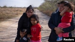 Dos solicitantes de asilo guatemaltecas con sus hijos esperan por transportación tras cruzar el Río Grande desde México a Texas, EE. UU., en una balsa el 10 de marzo de 2021.