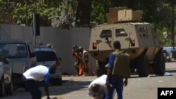 Bystanders look on as security personnel move beside an armoured personnel carrier in Ouagadougou on March 2, 2018, as the capital of Burkina Faso came under multiple attacks targeting the French embassy, the French cultural centre and the country's milit