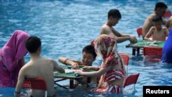 People play mahjong as they sit in water at a water park on a hot day in Chongqing, China August 2, 2017. 