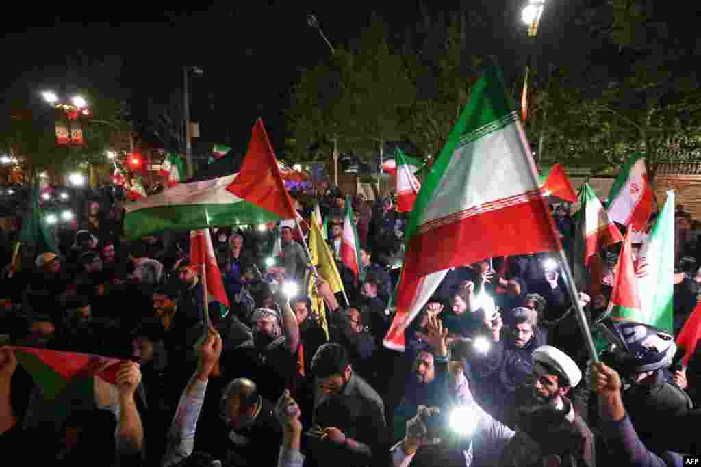 Demonstrators wave Iran's flag and Palestinian flags as they gather in front of the British Embassy in Tehran, April 14, 2024, after Iran launched a drone and missile attack on Israel.