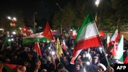 2024年4月14日，伊朗对以色列发动无人机和导弹袭击后，示威者聚集在英国驻德黑兰大使馆前，挥舞着伊朗国旗和巴勒斯坦国国旗。