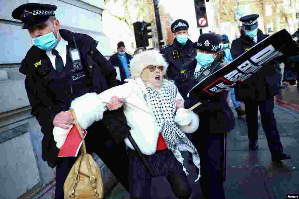Police officers detain a woman holding a placard outside the Westminster Magistrates Court as Julian Assange's lawyers seek bail for their client in London.