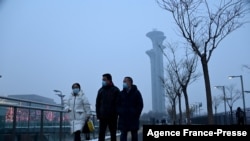 People walk along a path as the Beijing Olympic Tower is seen during a smoggy day in Beijing, Jan. 24, 2022. 
