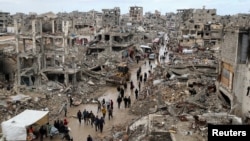 Палестинци поминуваат покрај урнатините на зградите уништени за време на израелската офанзива, на дождлив ден во градот Газа во услови на прекин на огнот меѓу Израел и Хамас, 6 февруари 2025 година 