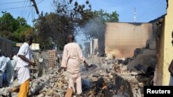 Residents watch as two men walk amidst rubble after Boko Haram militants raided the town of Benisheik, west of Borno State capital Maiduguri, Sept. 19, 2013.