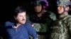 En esta foto de archivo del 8 de enero de 2016, Joaquín "El Chapo" Guzmán esposado se enfrenta a la prensa mientras es escoltado a un helicóptero por soldados e infantes de marina mexicanos en un hangar federal en la Ciudad de México.