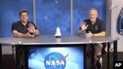 In this frame grab from NASA TV video, astronauts Bob Behnken, left, and Doug Hurley wave during a news conference, Tuesday, Aug. 4, 2020, in Houston. (NASA TV via AP)
