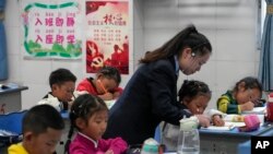 資料圖片：2023年9月5日，在媒體組織的四川省甘孜州稻城縣的參觀活動中，香格里拉鎮重點寄宿制學校一年級的一名老師在幫助一名學生寫字母。 （美聯社）