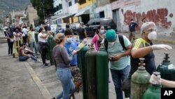 La gente espera con sus tanques de oxígeno vacíos afuera de una tienda de recarga, para llevárselos a sus familiares con COVID-19 en Caracas, Venezuela. Abril 9, 2021.