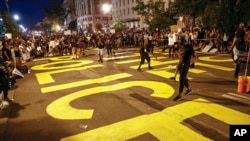 Demonstrators paint the words 'defund the police' as they protest Saturday, June 6, 2020, near the White House in Washington.