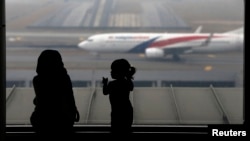 ស្ត្រី​និង​ក្មេង​ស្រី​ម្នាក់​មើល​យន្តហោះ​​មួយ​របស់​ក្រុមហ៊ុន​អាកាសចរណ៍​ម៉ាឡេស៊ី​​មួយ​គ្រឿង​ដែល​កំពុង​បើក​លើ​ផ្លូវ​នៅ​អាកាសយានដ្ឋាន​អន្តរជាតិ​គូឡាឡាំពួ។ (រូប​ឯកសារ)