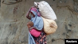A displaced Somali woman carries a child and her belongings after fleeing famine in the Marka Lower Shebbele regions, as she arrives at a temporary dwelling in the capital Mogadishu.