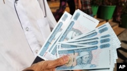 FILE - A man shows new currency notes outside Myanmar Economic Bank Tuesday, Jan. 7, 2020, in Yangon, Myanmar. In an order by Myanmar’s central bank Sunday, April 3, 2022, all foreign currency holdings must be converted into the local currency causing man