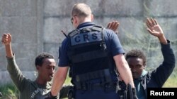FILE - A French riot policeman approaches migrants who are on their knees as French authorities block their access to a food distribution point in Calais, France, June 1, 2017. 