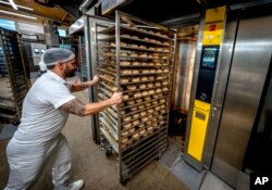 An employee pushes bread rolls into one of the gas heated ovens in the producing facility in Cafe Ernst in Neu Isenburg, Germany, Monday, Sept. 19, 2022. Andreas Schmitt, head of the local bakers' guild, said some small bakeries are contemplating giving up due to the energy crisis. (AP Photo/Michael Probst)