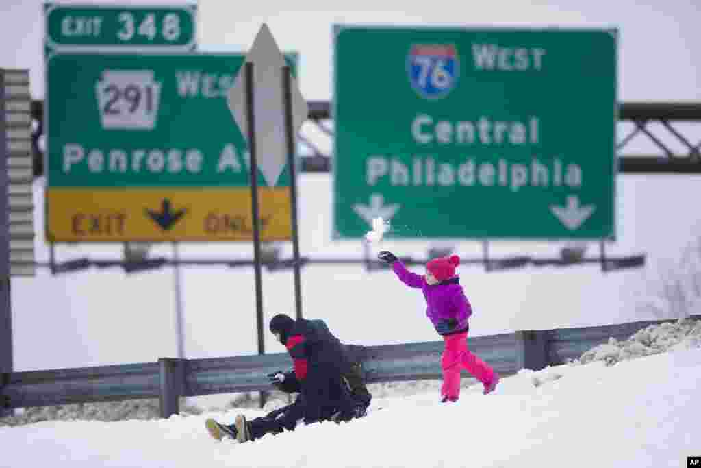 A young girl tosses snow from an Interstate 76 embankment as she and others play, Feb. 13, 2014, in Philadelphia. 